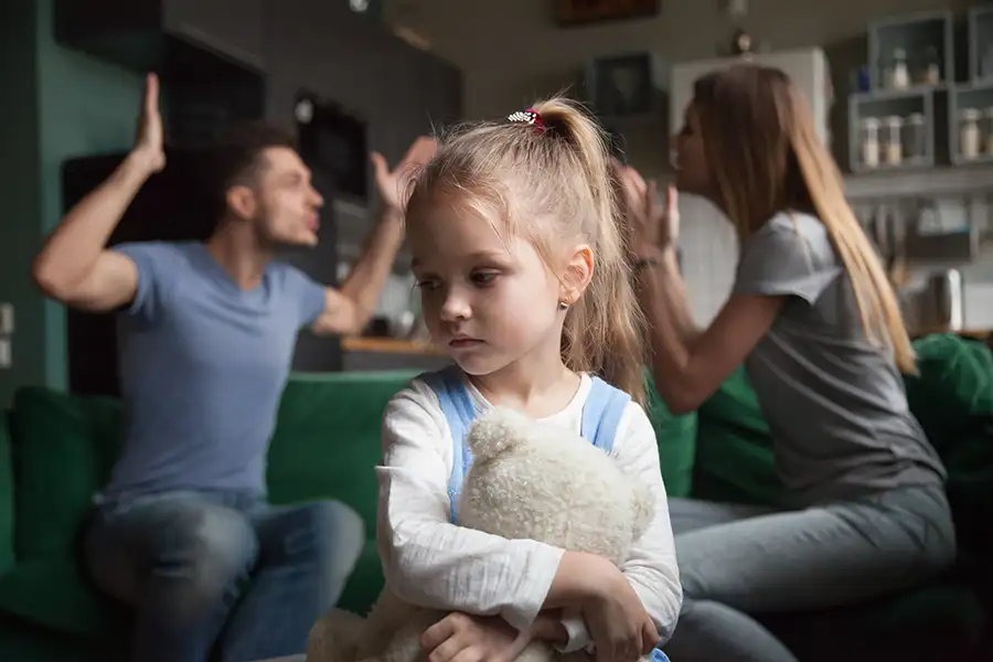 Child of divorce concept - little girl with stuffed bear sits sadly listening to her parents fight - Schuyler County IL